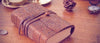 Journal intime cuir posé sur une table en bois avec montre à gousset et pomme de pin