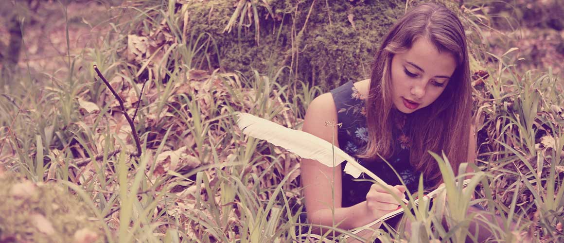 femme qui écrit un journal intime avec une plume dans l'herbe dans la forêt